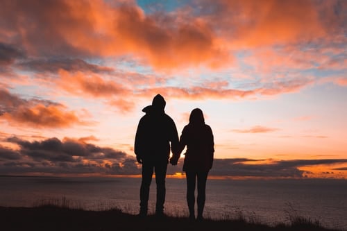 Silhouettes of two people holding hands in front of a sunset