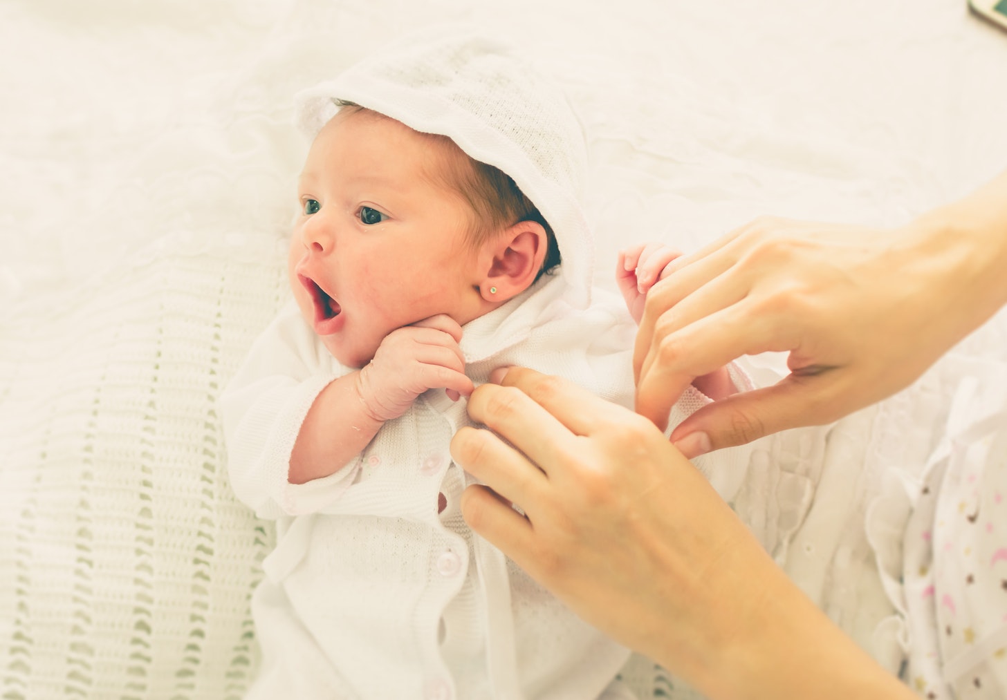 Baby girl being dressed into a white hoodie.