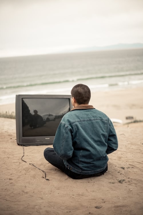 Person sitting at the beach looking at an old tv