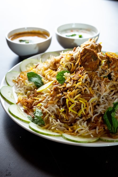 Mutton biryani on a plate surrounded by sliced cucumber